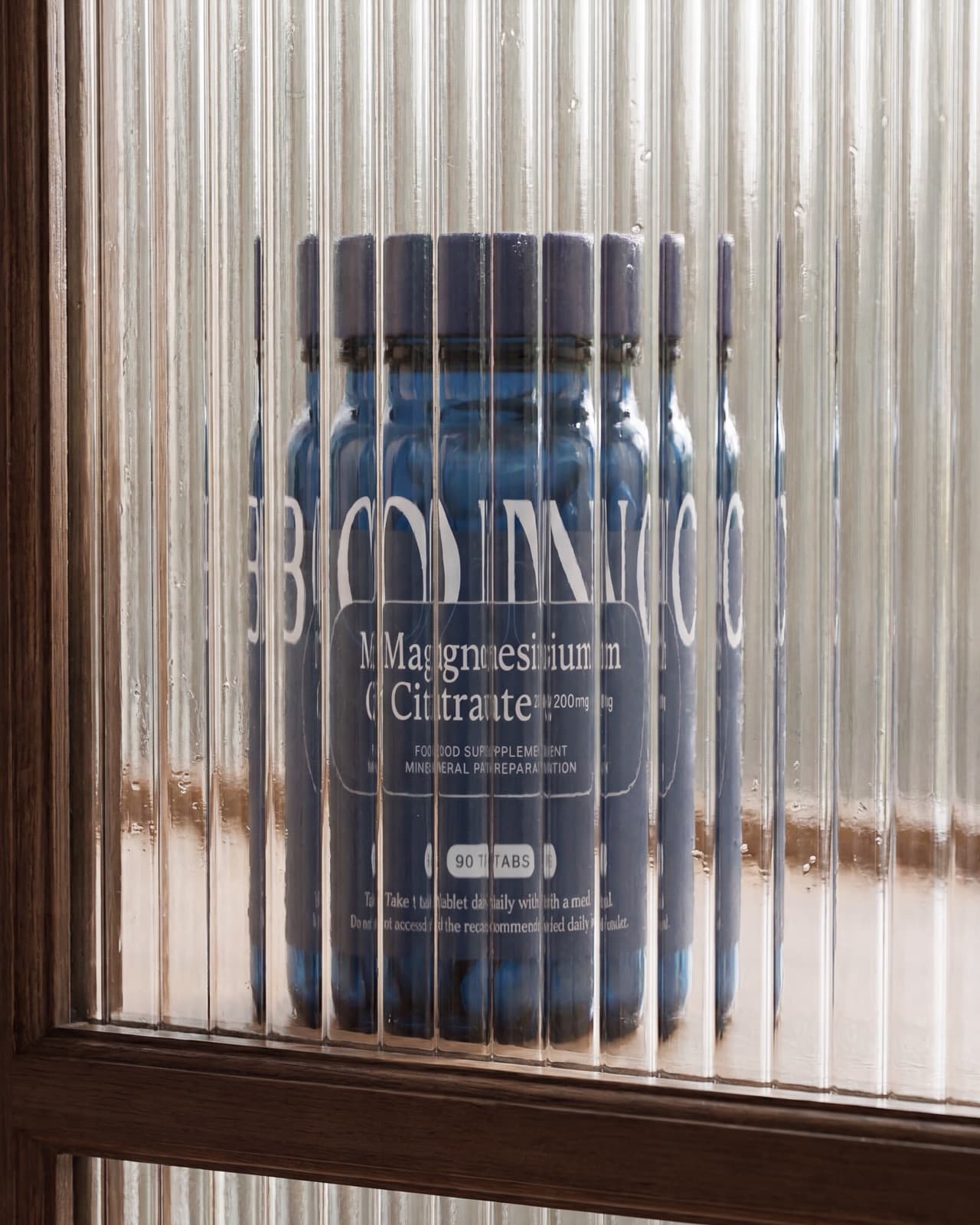 Een pot BONO Supplements Magnesium Citraat achter geribbeld glas